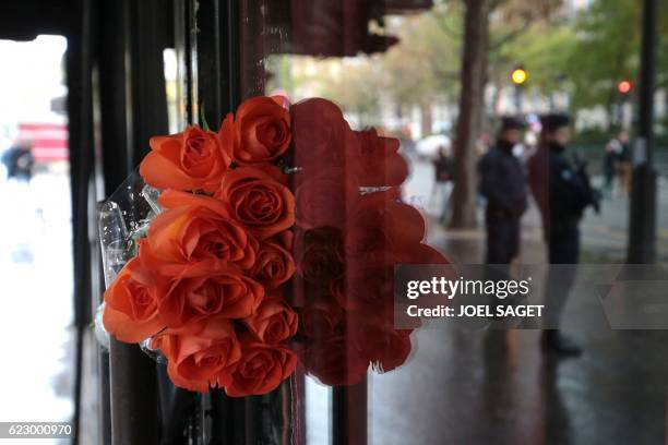 This picture taken on November 13, 2016 shows the reflection of policemen in the front door of the Bataclan Cafe in Paris where flowers were laid,...