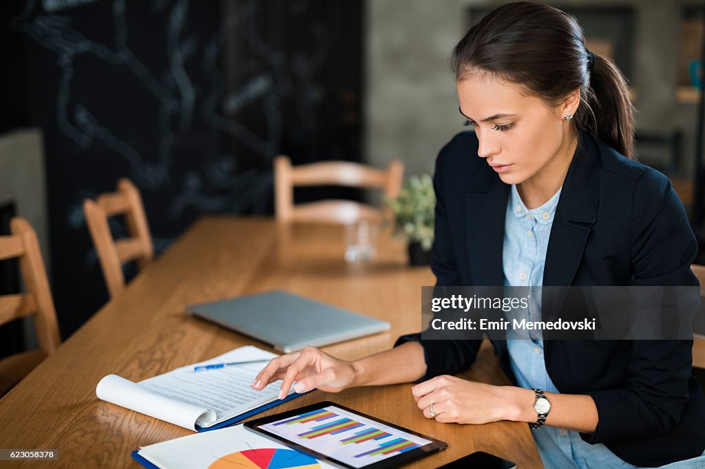 Young businesswoman using digital tablet and analyzing business report.