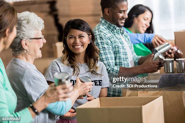 volunteers pack canned goods into boxes during food drive - recolha-de-alimentos imagens e fotografias de stock