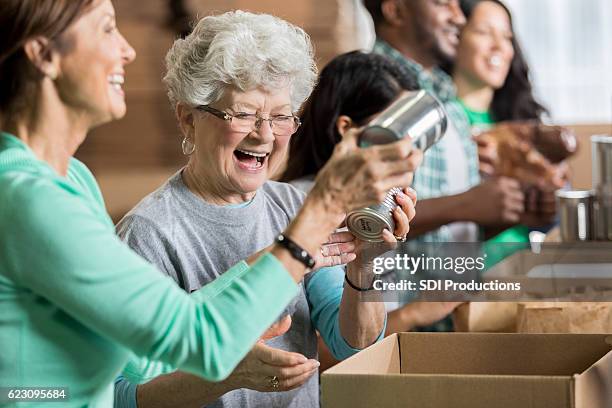 happy female friends volunteer at charity food bank - recolha-de-alimentos imagens e fotografias de stock