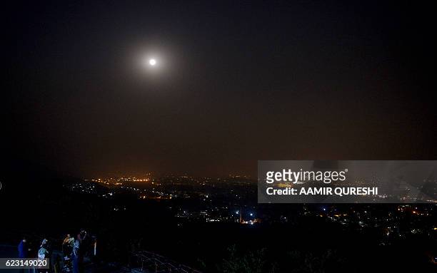 Pakistani people watch the 'supermoon' rise over the skyline of Islamabad on November 14, 2016. Skygazers headed to high-rise buildings, ancient...