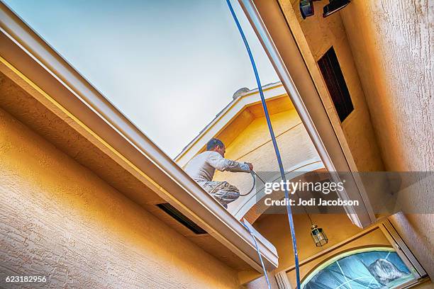 series:house painter standing on roof spray painting entryway trim - painted roof stock pictures, royalty-free photos & images