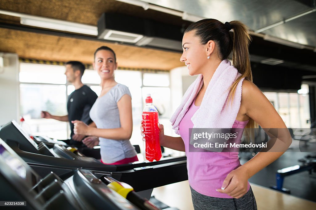 Mujer joven que sostiene una bebida refrescante mientras hace ejercicio en la cinta de correr.