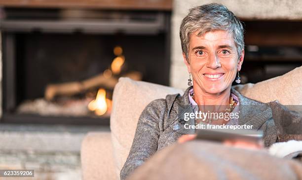 woman reading a tablet on the couch - haardvuur stockfoto's en -beelden