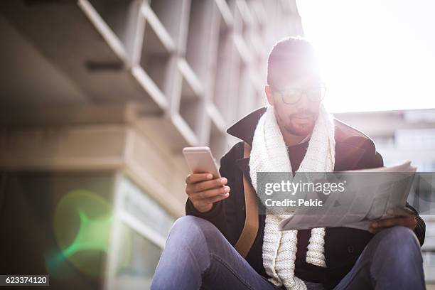 geschäftsmann liest zeitung und nutzt smartphone - junger mann liest zeitung stock-fotos und bilder