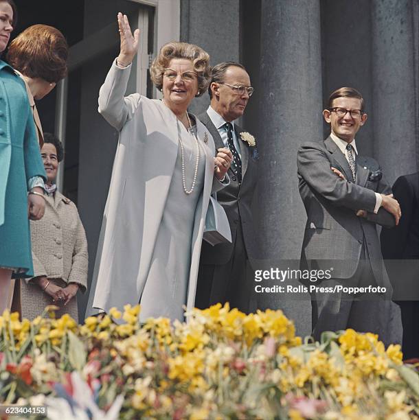 On the day of her 60th birthday, Queen Juliana of the Netherlands waves to crowds of spectators along with Prince Bernhard of Lippe-Biesterfeld and...