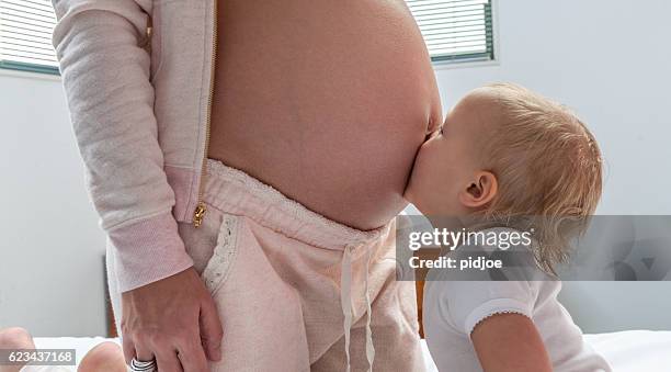 mother in advanced stages of pregnancy with daughter kissing belly - belly kissing stock pictures, royalty-free photos & images