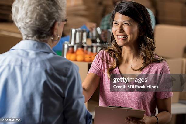 beautiful food bank organizer greets senior volunteer - agenda meeting stock pictures, royalty-free photos & images