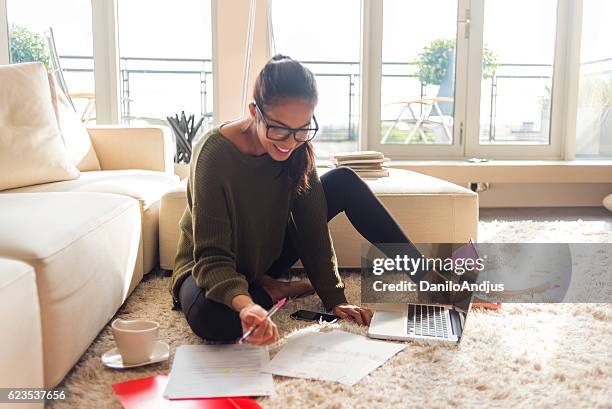 smiling young woman studying in her living room - student thinking stock pictures, royalty-free photos & images