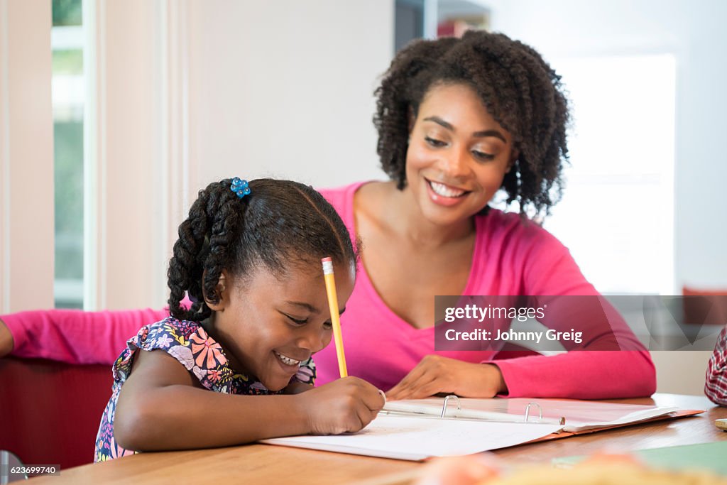 Jovem fazendo dever de casa com sua mãe sorrindo e assistindo