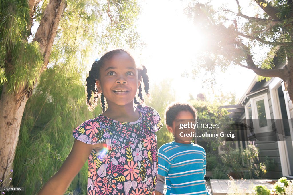 Young girl with her brother playing in garden sunlight