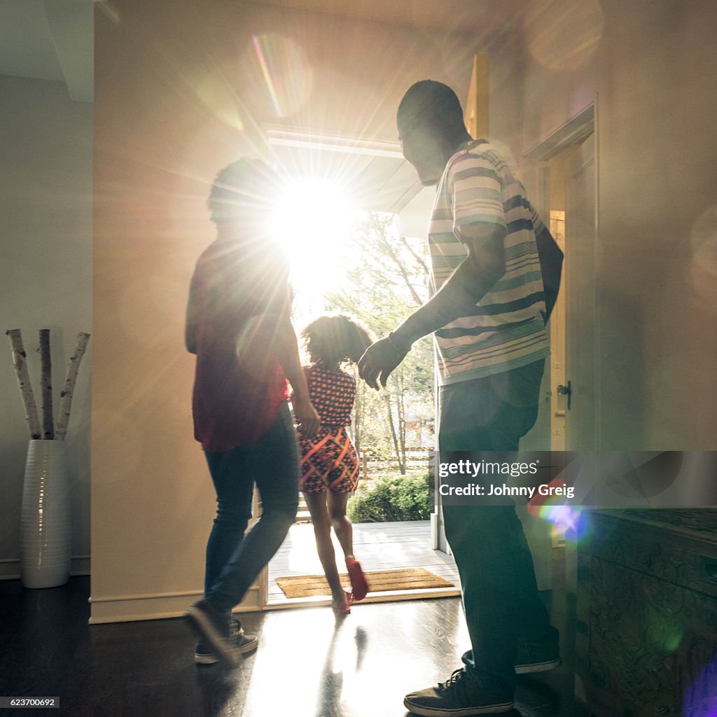 Parents with daughter leaving the house in bright sunlight