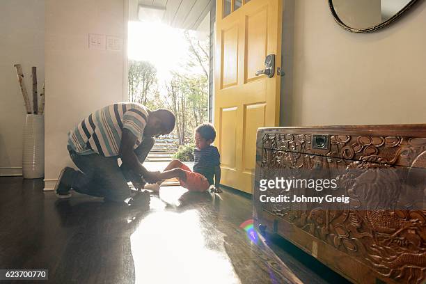 african american father helping son with shoes by front door - house entrance hall stock pictures, royalty-free photos & images