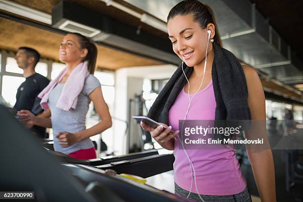 young woman using mobile phone while exercising on treadmill. - after workout towel happy stock pictures, royalty-free photos & images