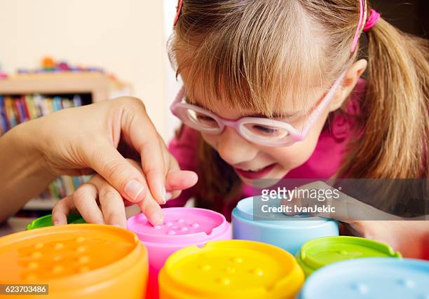 smiling child with disability touching textured cups with her teacher - sensory perception stock pictures, royalty-free photos & images
