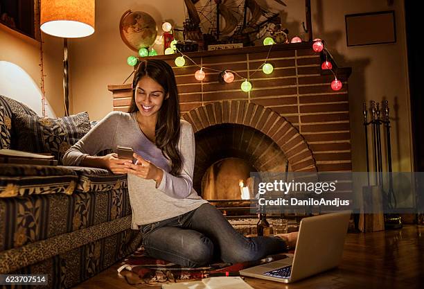 young woman using her smartphone sitting next to the fireplace - heat pad stock pictures, royalty-free photos & images