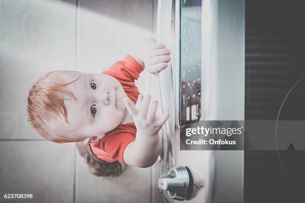 baby boy touching grabbing oven handle in kitchen - kitchen dresser stock pictures, royalty-free photos & images