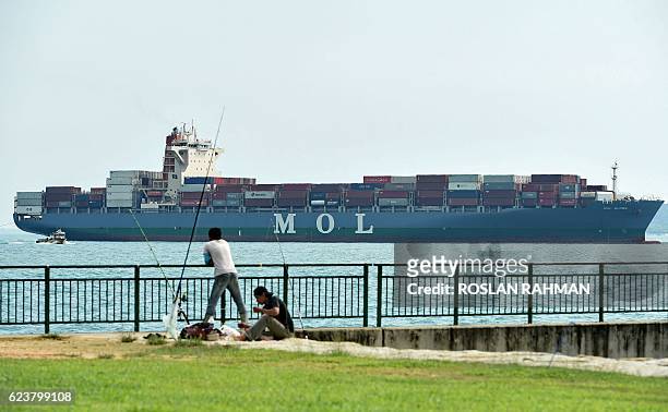 Two men catch fish in front of a container ship about to dock at Tanjong Pagar container port in Singapore on November 17, 2016. Singapore's exports...