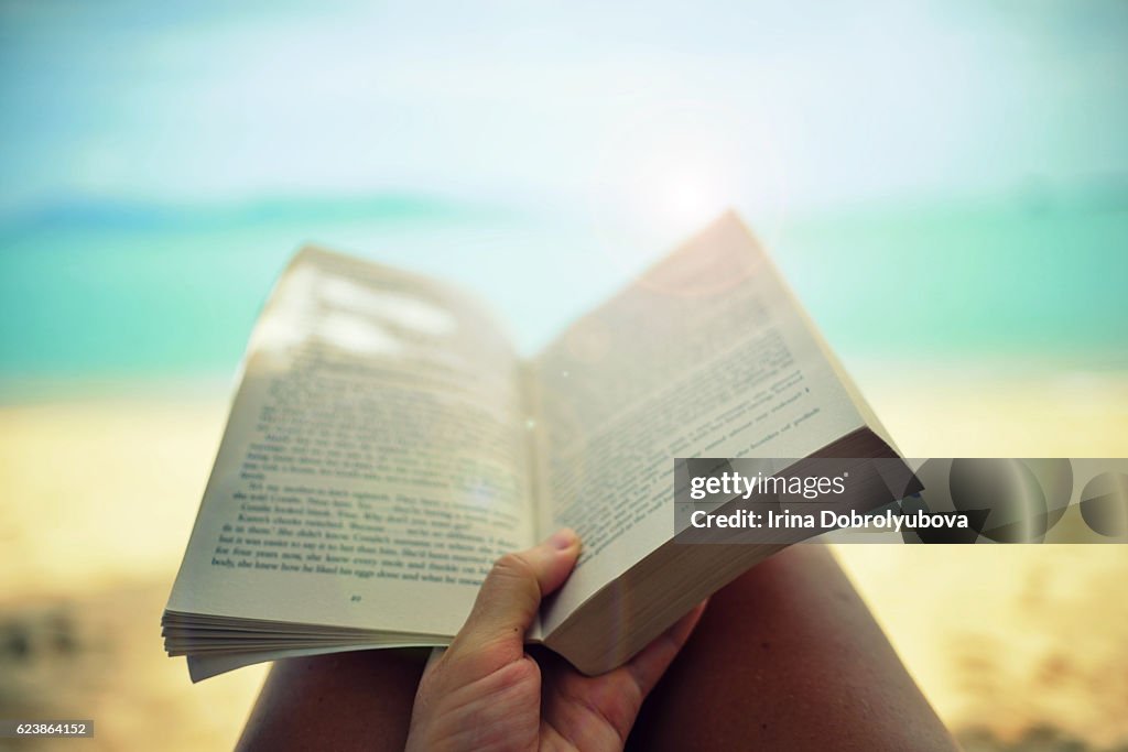 Reading paper book on the beach from personal perspective