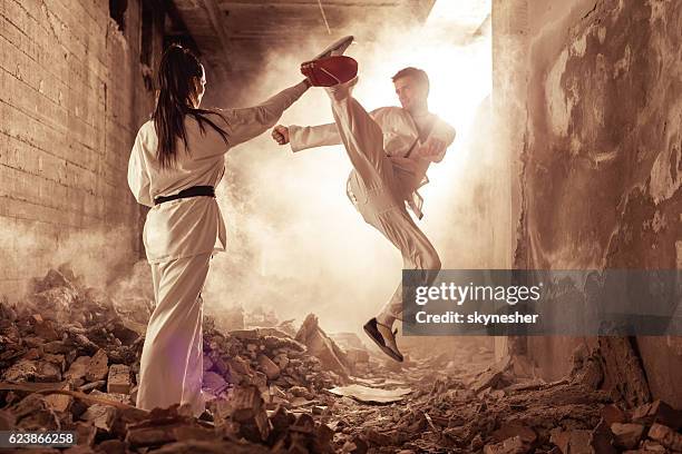 taekwondo fighter practicing high kick with help of sparring partner. - high kick stock pictures, royalty-free photos & images