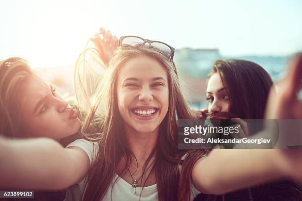 groupe de filles souriantes prenant drôle selfie en plein air au coucher du soleil - blonde fille photos et images de collection