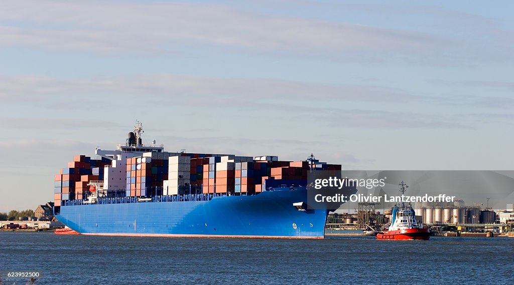 Blue containership with containers being tugged in the Rotterdam harbour