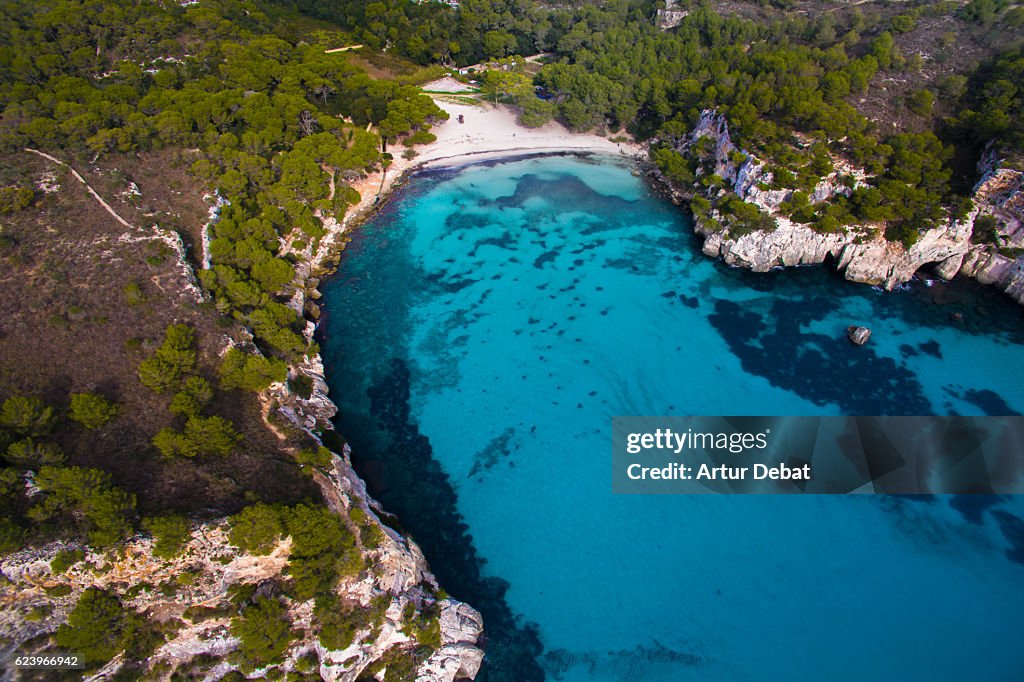 Aerial picture taking with drone flying over the beautiful Menorca island in the Cala Macarella beach with nice turquoise water and stunning landscape.