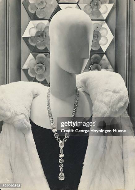 Mannequin with simplified head and face, wearing black dress and white fur coat with large collar, both designed by Worth; and necklace of large...