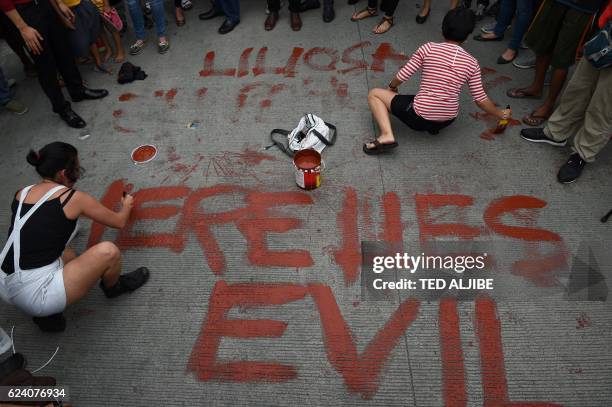 Anti-Marcos protestors paint the street with anti-Marcos slogan during a protest in front of the gates of the heroes' cemetery while the late...