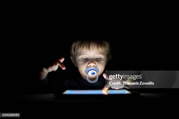 1 year old boy looking a digital tablet in the dark - dark baby stock pictures, royalty-free photos & images