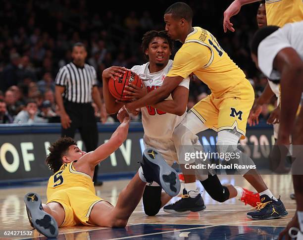 Ben Moore of the Southern Methodist Mustangs fights for a loose ball with D.J. Wilson and Muhammad-Ali Abdur-Rahkman of the Michigan Wolverines in...