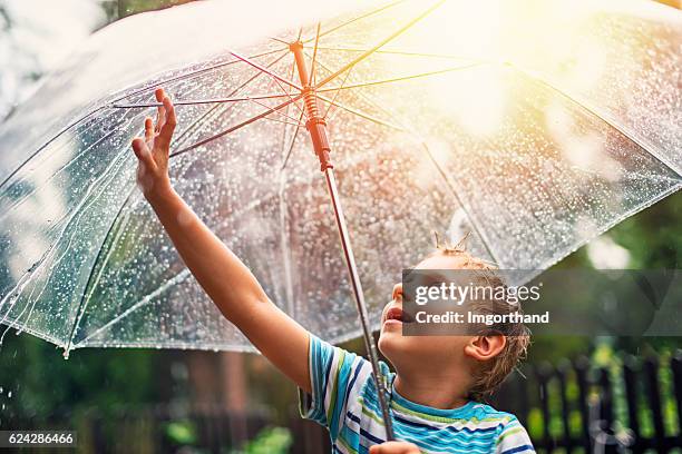 kleiner junge mit transparentem regenschirm, der regen genießt. - regen sonne stock-fotos und bilder