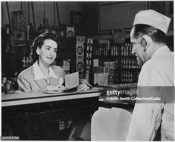 During World War II, a wife and mother presents her ration book to the butcher behind the counter of a deli, Hyde Park, New York, 1943. .