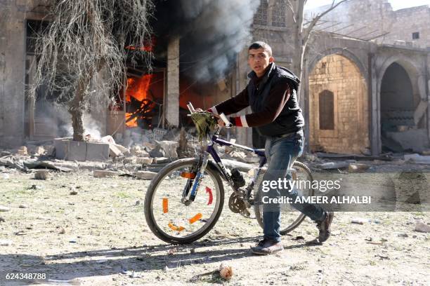 Syrian youth pushes his bicycle past a burning house on November 19, 2016 following a reported air strike on Aleppo's rebel-held neighbourhood of Bab...