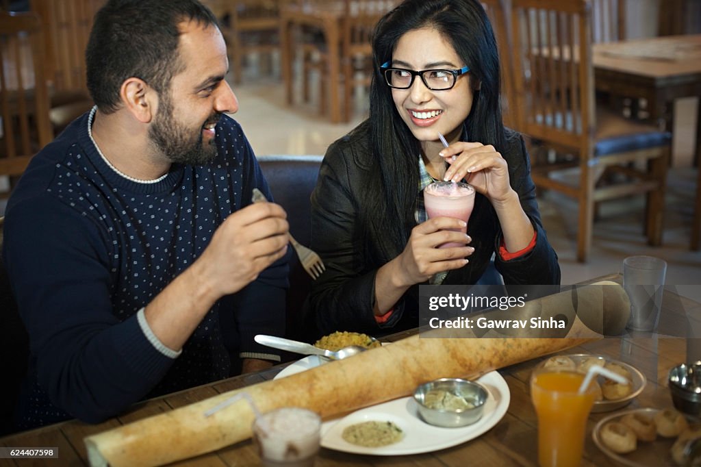 Multi ethnic young couple eating south Indian food at restaurant.