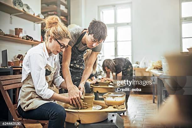 man and woman in workshop working on pottery wheel - potters wheel stock pictures, royalty-free photos & images