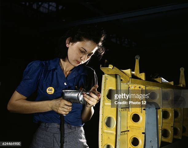 American female engineer during World War II, drilling horizontal stabilizers using operating a hand drill. The woman is working on the horizontal...