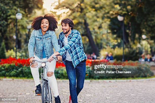 multi ethnic couple with a bike - adult riding bike through park stock pictures, royalty-free photos & images