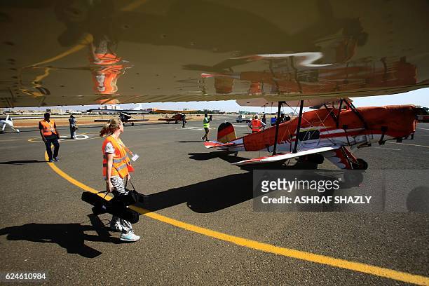 Officials walk past the vintage Bucker Bu 131 biplane as it sits on the runway on November 20, 2016 in Khartoum airport during the Vintage Air Rally...