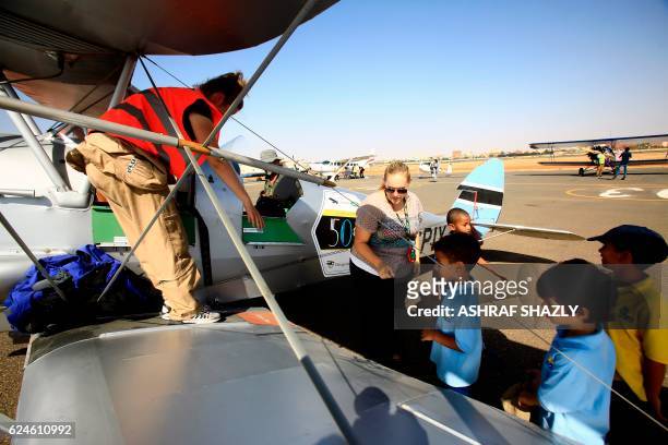Children line up to sit inside the vintage de Havilland Tiger Moth biplane as it sits on the runway on November 20, 2016 in Khartoum airport during...