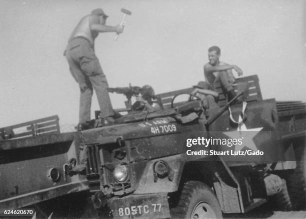 Photograph of four United States Army serviceman amusing each other on a parked M35 military truck, two of the soldiers watch in amusement while a...