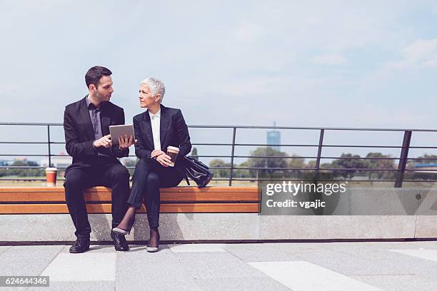 businesspeople sitting on the bench and using digital tablet. - man lady phone ipad outside stock pictures, royalty-free photos & images