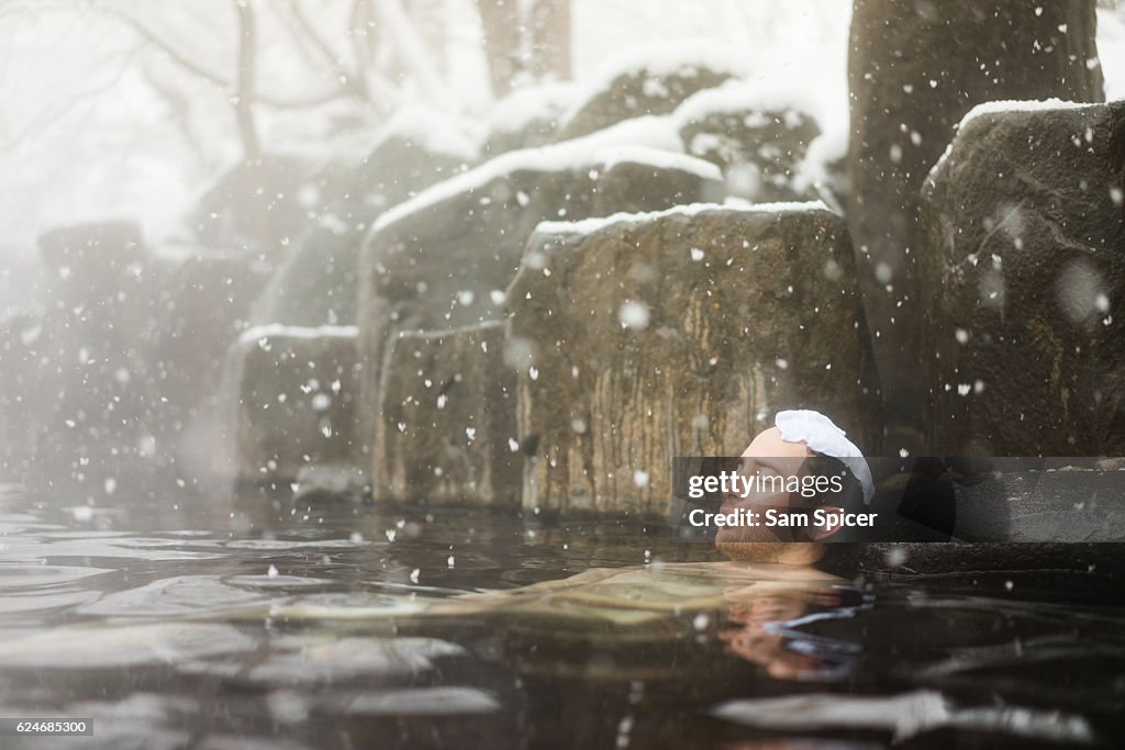 Western tourist enjoying natural hot spring onsen during Winter snow