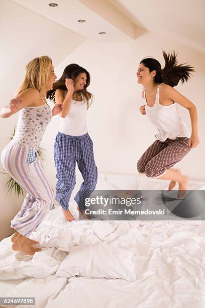 les femmes enjoués s’amusent à la fête de sommeil en sautant sur le lit - vêtement de nuit photos et images de collection