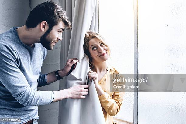 young happy couple fooling around with curtain at home - kid hide and seek stock pictures, royalty-free photos & images