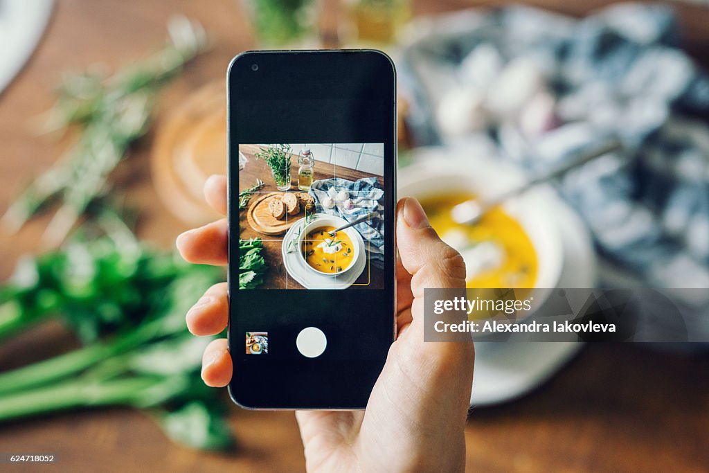 Frau macht Foto von Kürbissuppe mit Smartphone