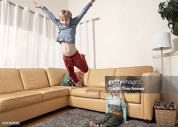 young boy jumping off couch with little brother. - stoeien stockfoto's en -beelden