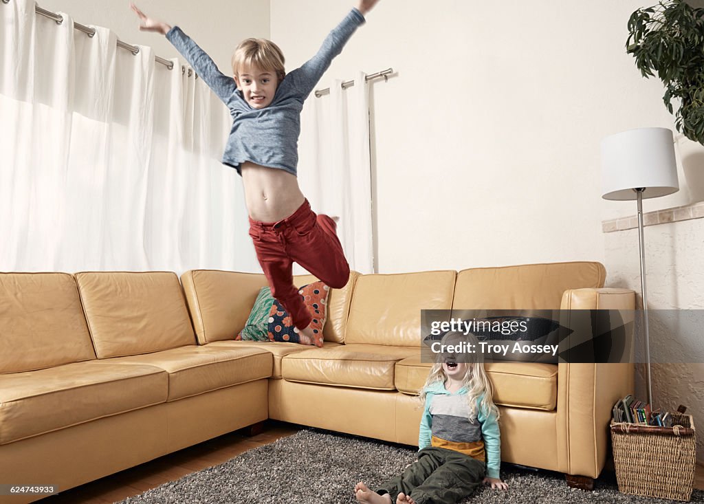 Young boy jumping off couch with little brother.