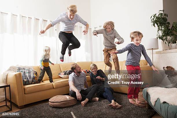 kids jumping off couch over parents. - fyrbarnsfamilj bildbanksfoton och bilder