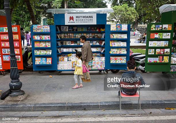 Sale of books on mobile sales stall on a street in Hanoi. In the foreground a young man sits on a chair on October 30, 2016 in Hanoi, Vietnam.